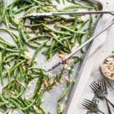 a pan of roasted green beans from overhead with a set of tongs on top