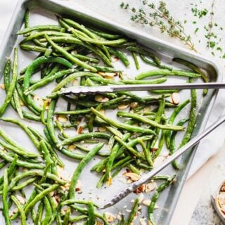 a pan of roasted green beans from overhead with a set of tongs on top