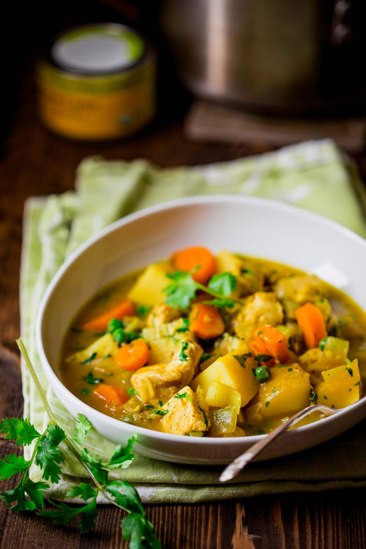 side view of a white bowl of hearty chicken, potato and vegetable curry with peas and cilantro on a green dish towel.