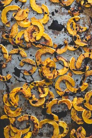 overhead of delicata squash half-moons on a baking sheet with drizzled reduction