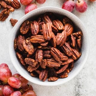 Spiced nuts in a white bowl with red grapes