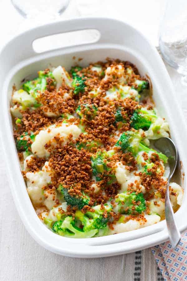a white casserole dish with broccoli and cauliflower casserole with browned breadcrumbs on top with a spoon in it