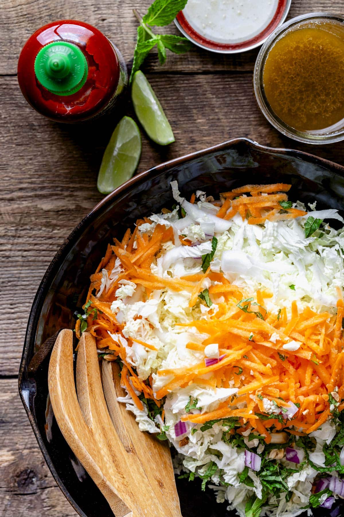 the slaw in a bowl with the dressing on hand and a bottle of sriracha