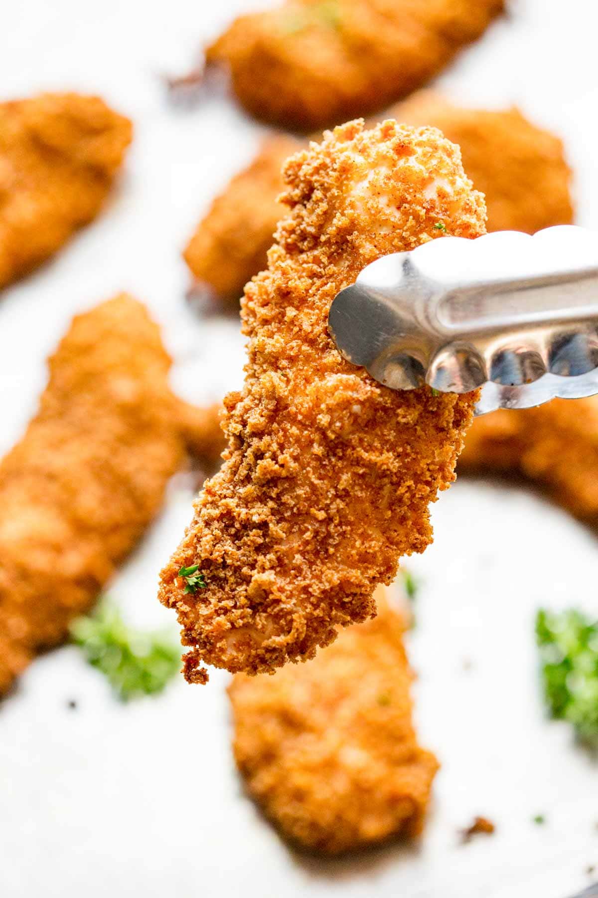 close up of a chicken tender in tongs