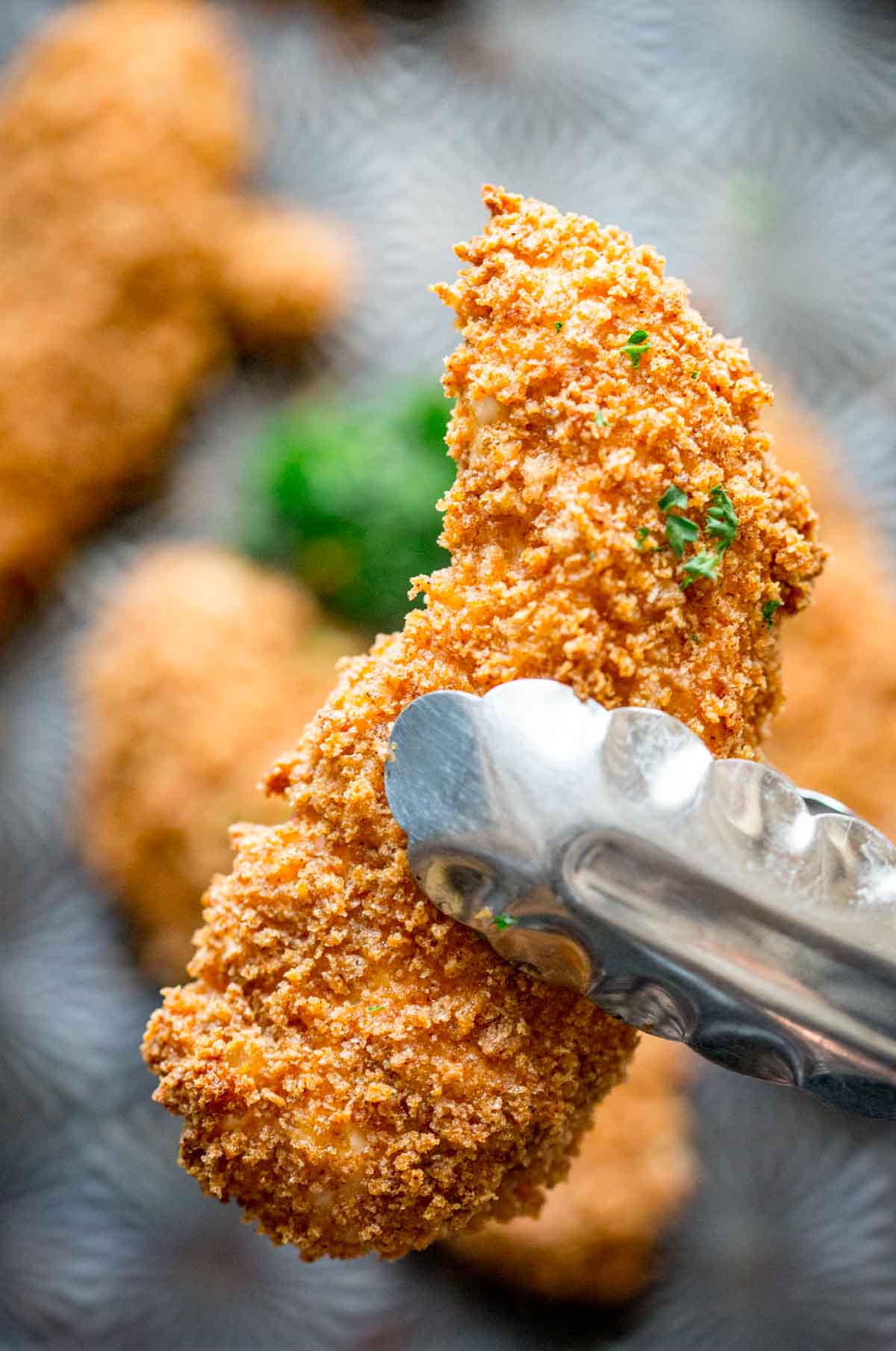 a chicken tender in tongs with a dark background