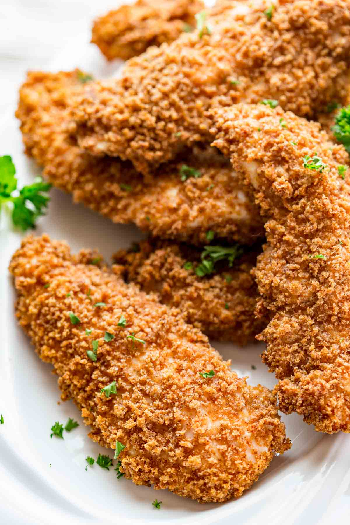 white plate with a pile of baked breaded chicken tenders on it