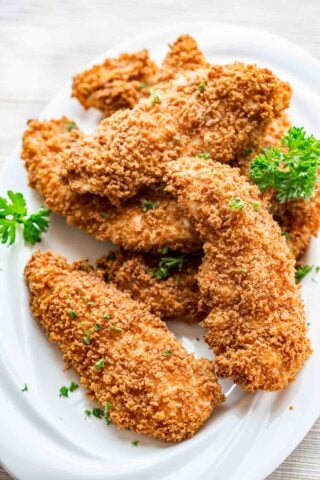 white plate with a pile of baked breaded chicken tenders on it