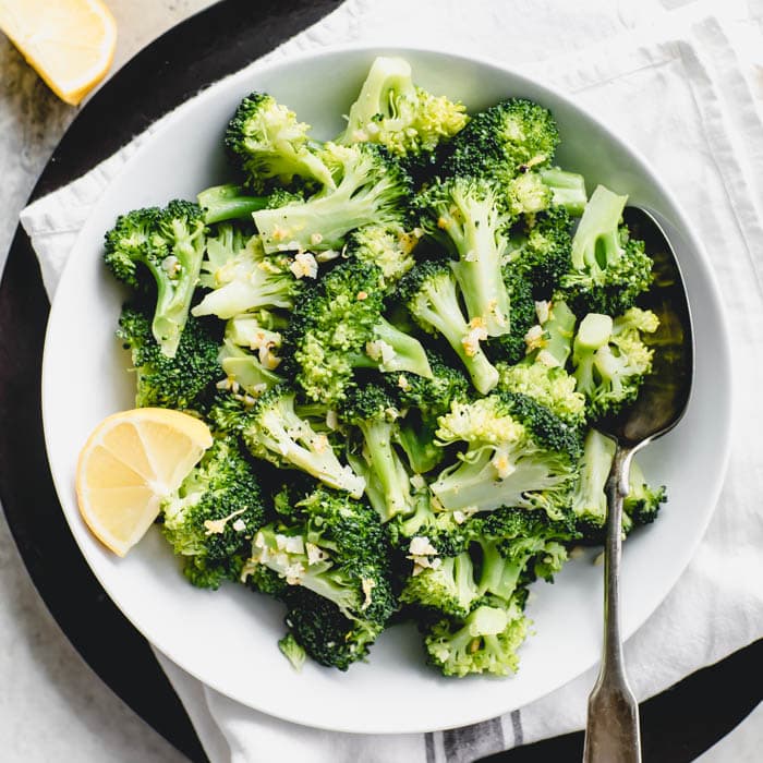 overhead closeup of broccoli in a white bowl with a lemon wedge