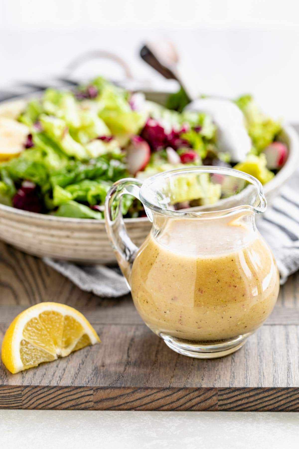a pitcher of dressing with salad behind it
