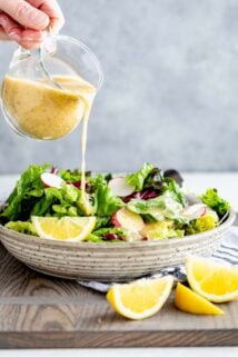 pouring lemon dressing over a salad