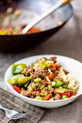 ground pork stir-fry in a white bowl with the wokbehind it