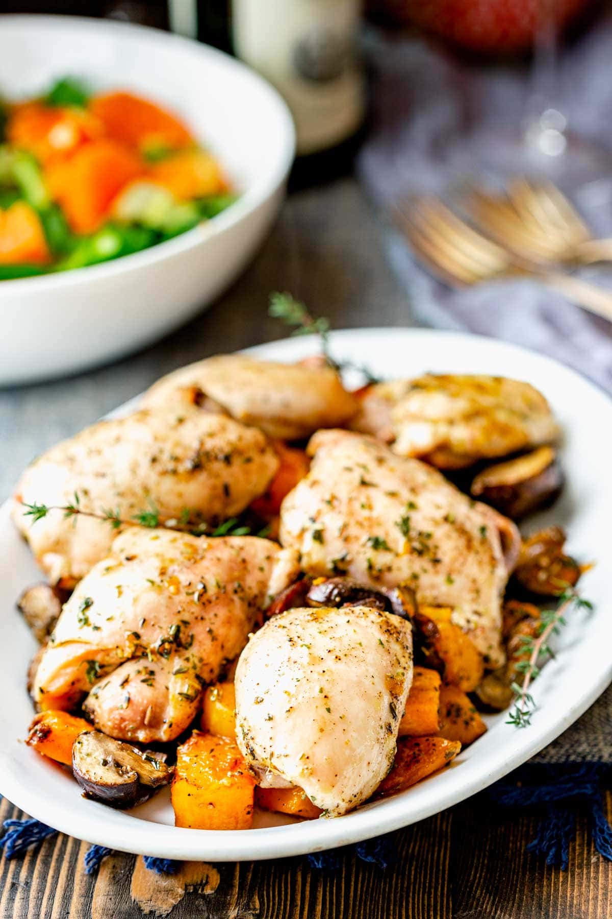 chicken thighs on a white platter with squash and salad in the backgroud