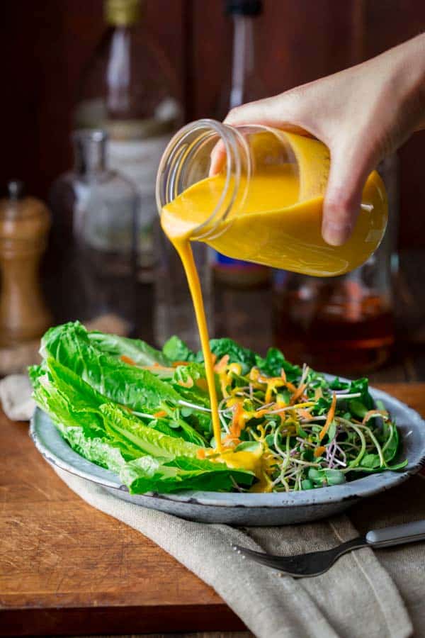 pouring carrot ginger dressing onto a salad