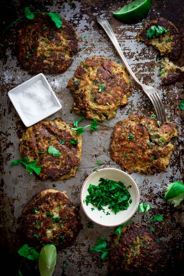 Mexican Cauliflower Patties on a tray with parsley in a bowl and sprinkled around them