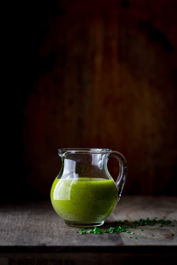 bright green chive oil vinaigrette in a clear pitcher with chopped chives on the table around it