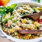 side view of the quinoa salad in a white view with wooden salad tongs