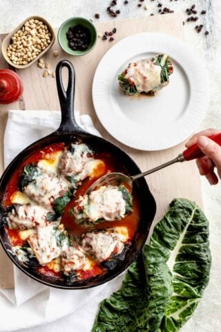 swiss chard rolls in a skillet, one is on a plate and another is being lifted up on a slotted spoon