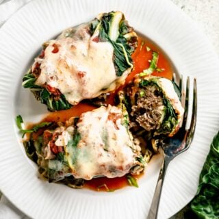 two Swiss chard rolls on a small plate and one is cut into so you can see the beef inside