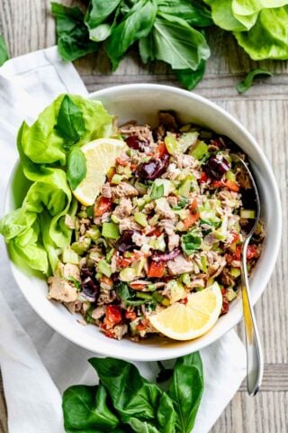 Mediterranean tuna salad in a white bowl with lemon wedges