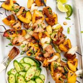 a tray of pork and peach kebabs with cucumber salad and limes