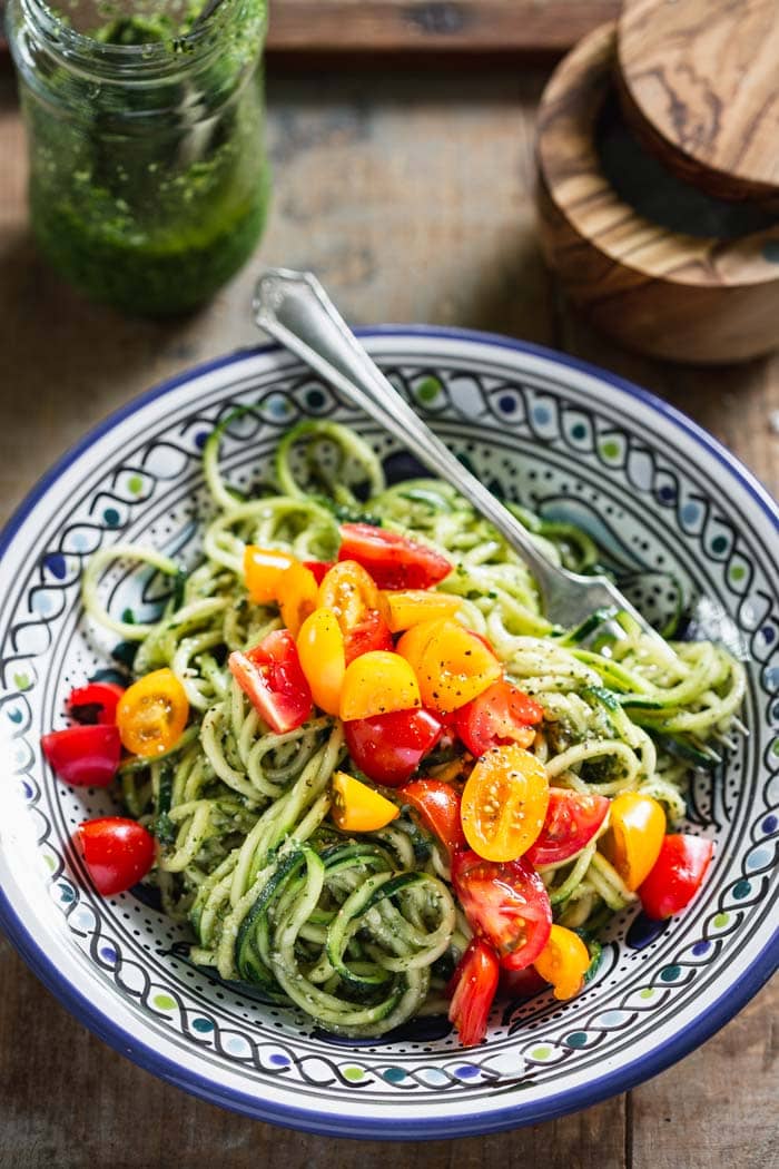 a blue bowl with a pile of green pesto zoodles with a fork in it