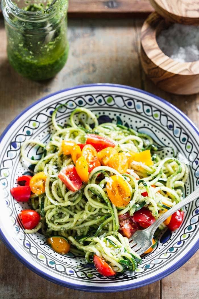A blue and white plate with zucchini noodles topped with colorful cherry tomatoes