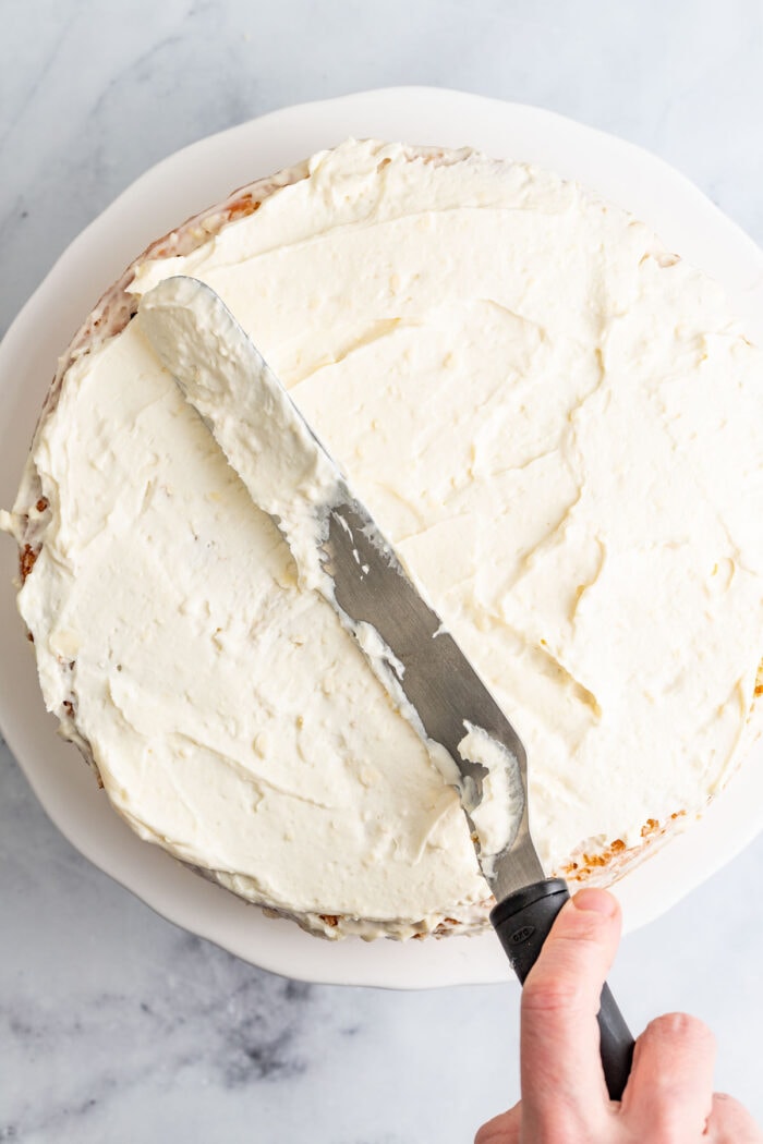 spreading cream cheese frosting over the cake and on the sides