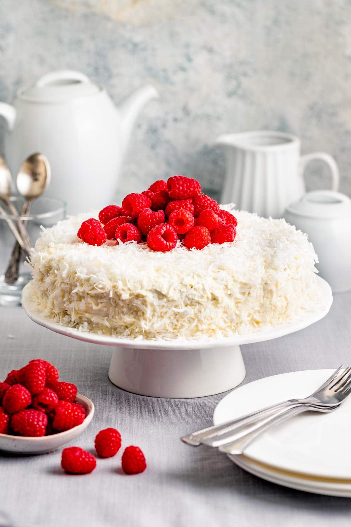 coconut cake with raspberries on top with a tea pot in the background