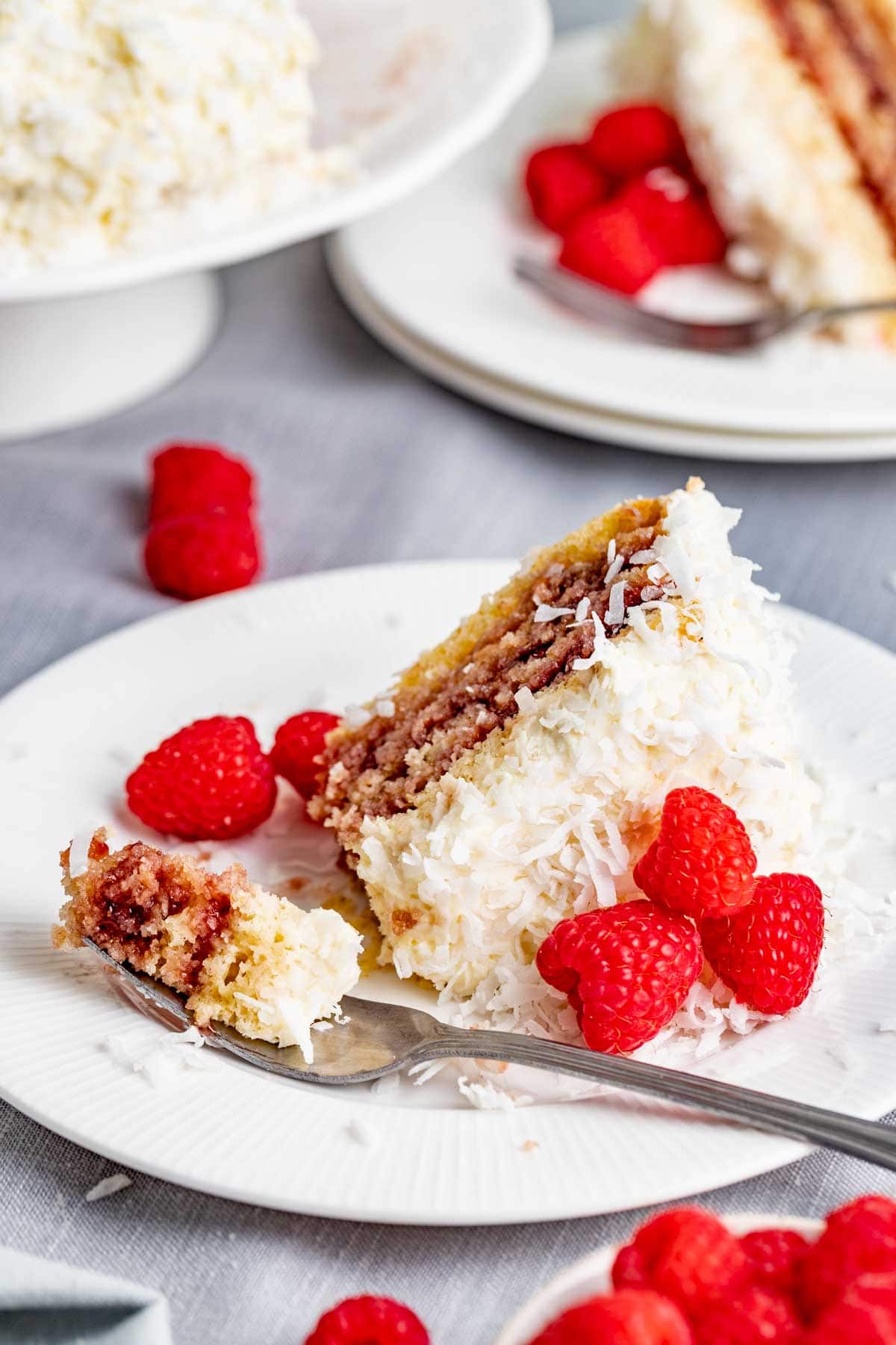 the cake slice on a plate with a bite resting on a fork with fresh raspberries