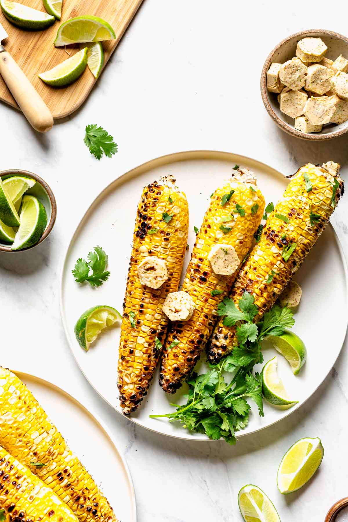 a plate of corn on the cob with cilantro and lime wedges