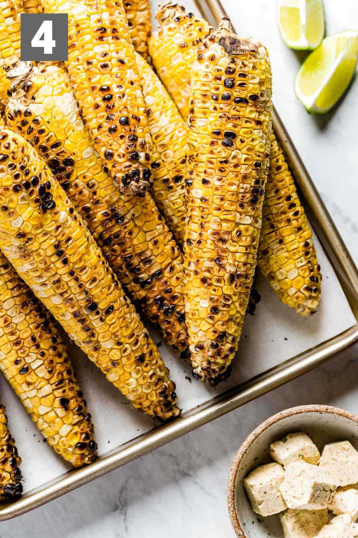 grilled corn with the flavored butter in a dish and lime wedges