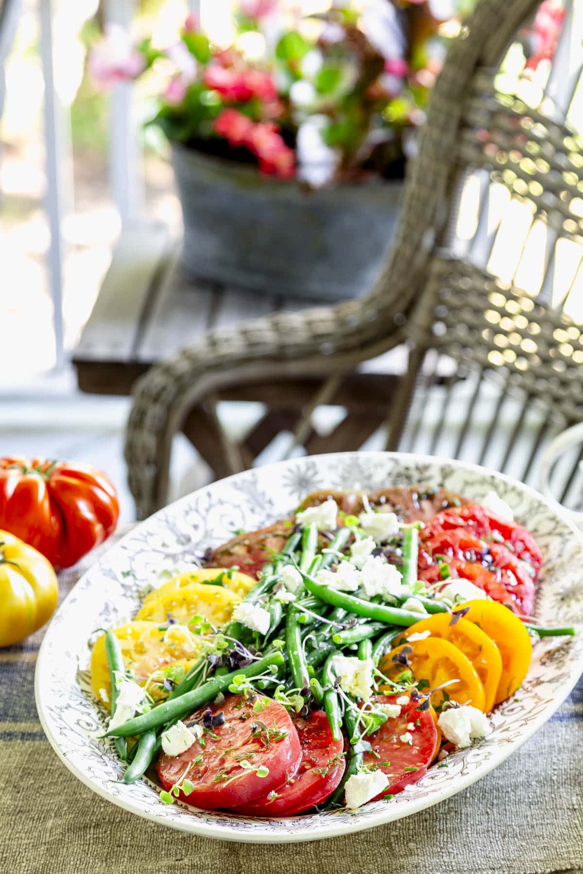 the plate with the salad on it with a rocking chair, tomatoes and a pot of flowers in the background.