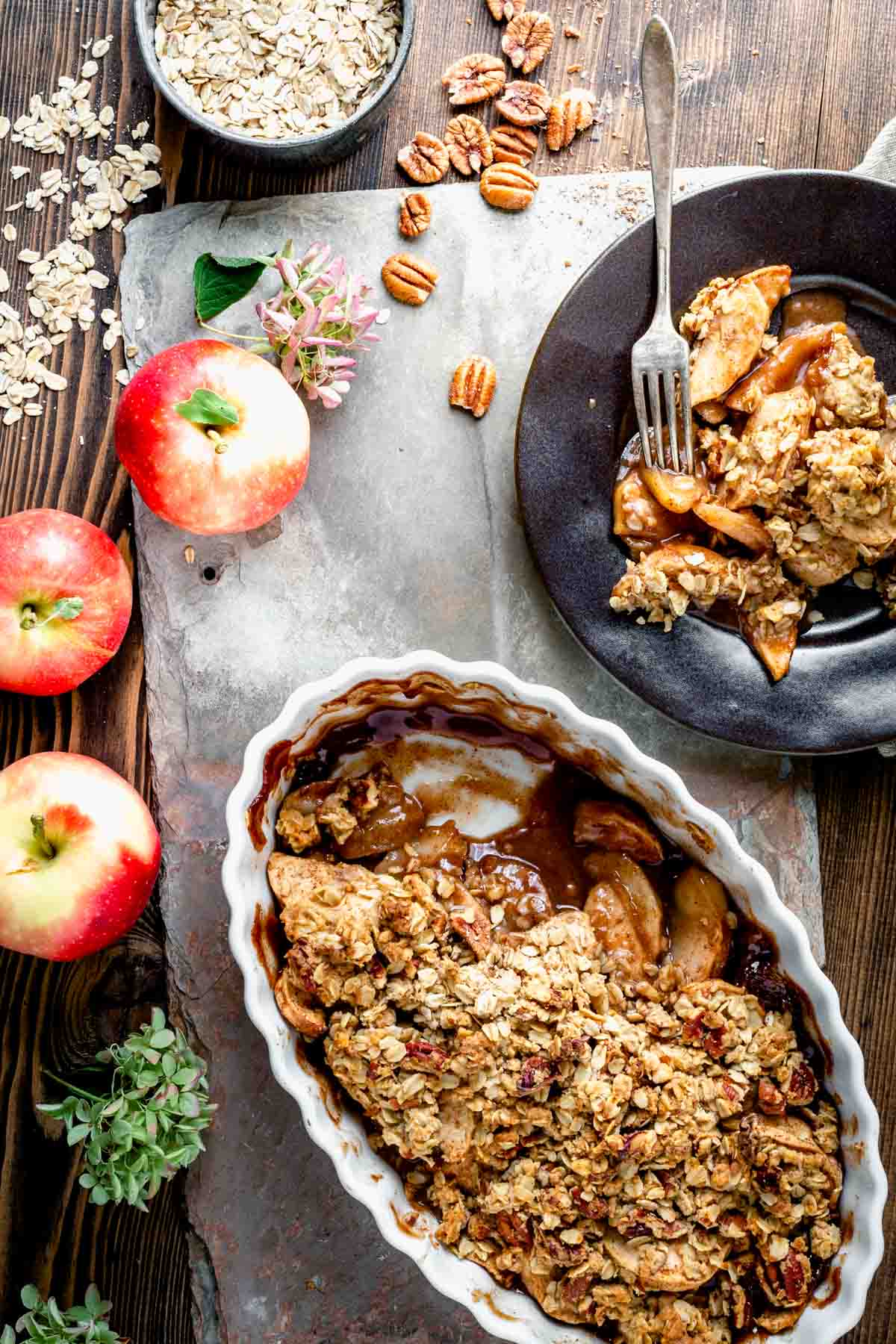 overhead tablescape with a crisp in a white ceramic dish, apples and a serving of the crisp on a black plate