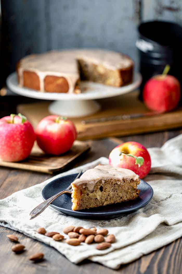 a slice of apple cake and a cake on a cake stand with apples in front