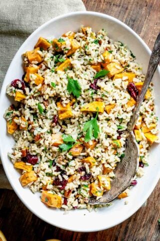 closeup of oval white bowl filled with brown rice salad with chunks of roasted sweet potatoes in it