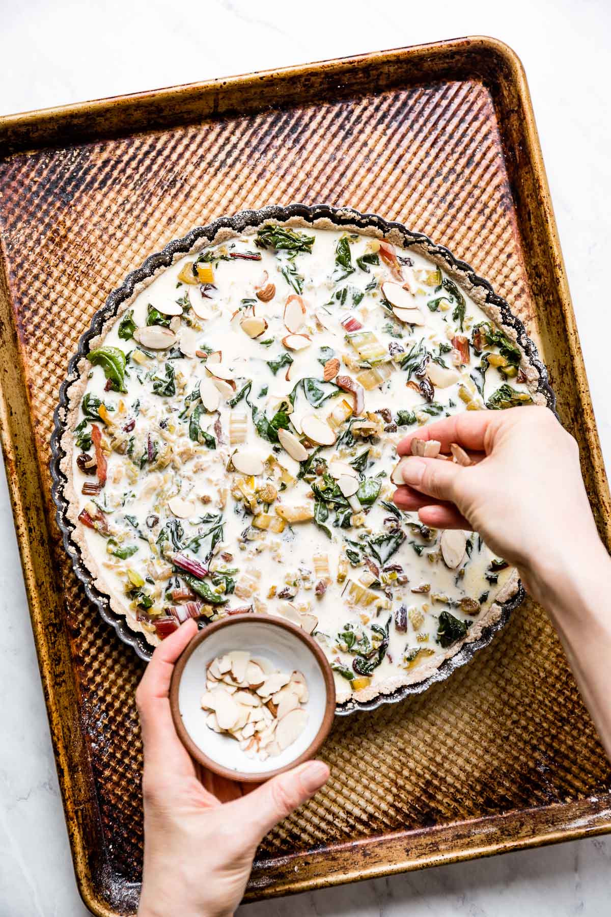 A person putting almonds on top of the tart