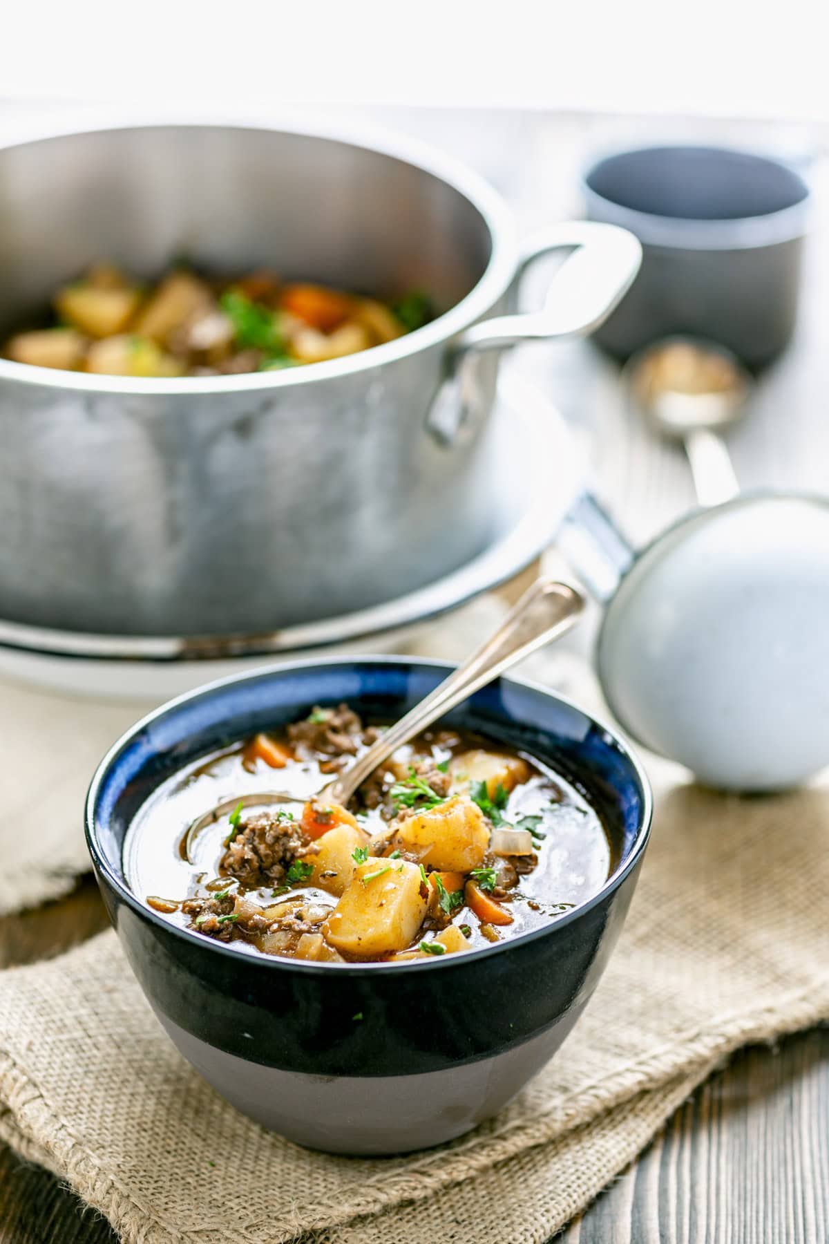the stew in a blue bowl with a spoon in it and the pot in the background