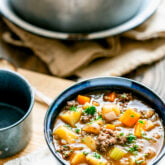 Delicious beef stew made with ground hamburger meat in a blue bowl with the soup pot in the background