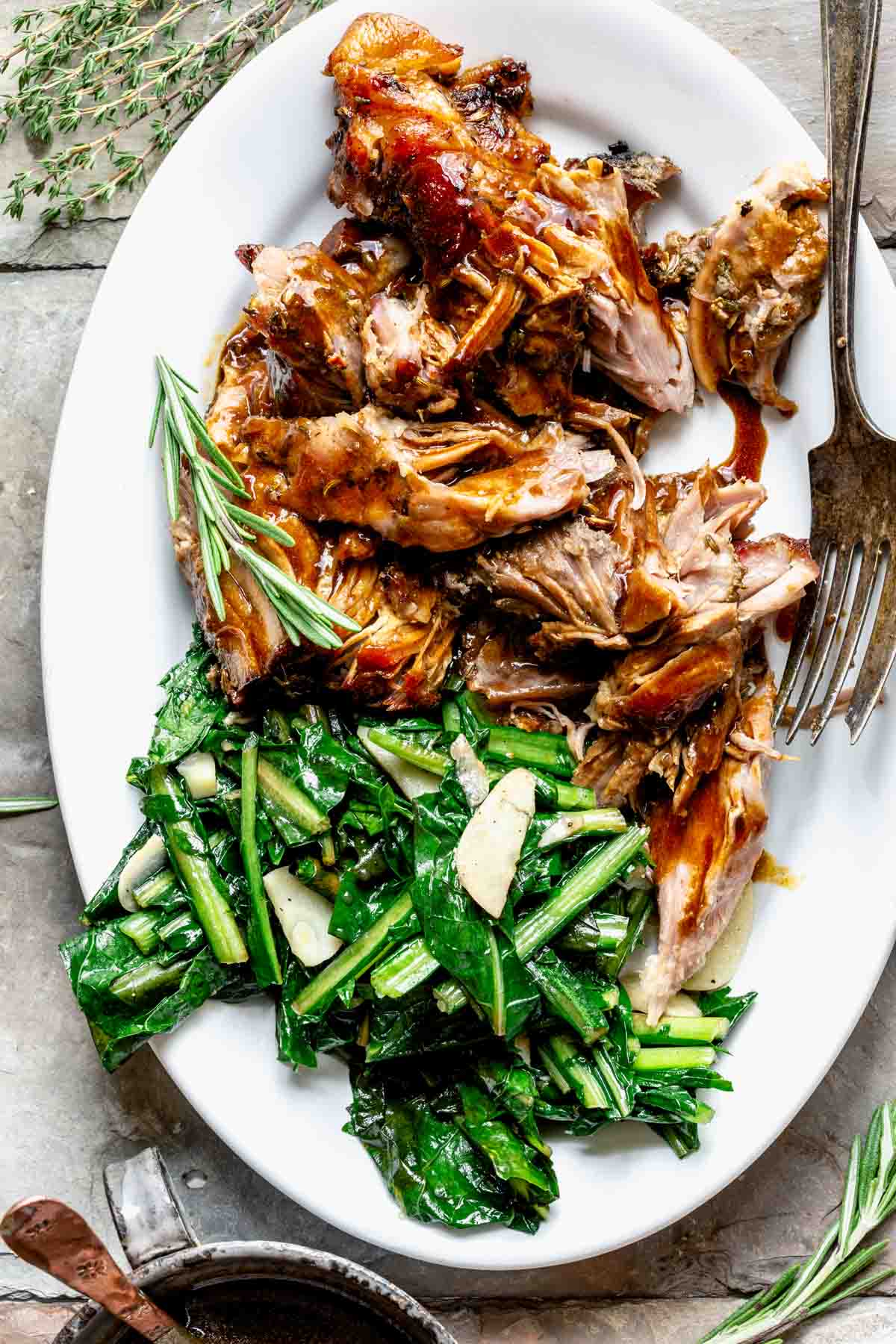 chunks of slow roasted pork with sauteed mustard greens and gravy drizzled on it on a white oval platter