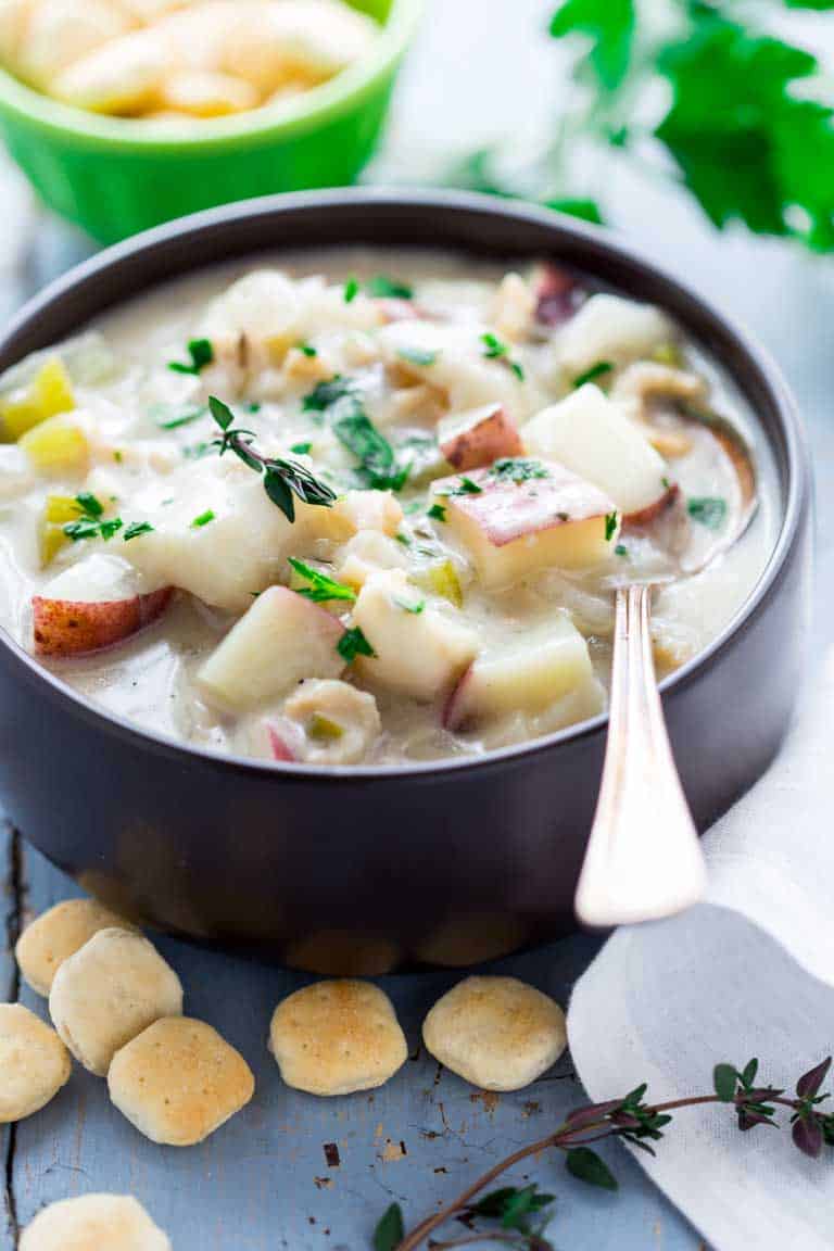 a black bowl of seafood chowder on a blue table with lots of oyster crackers on the table