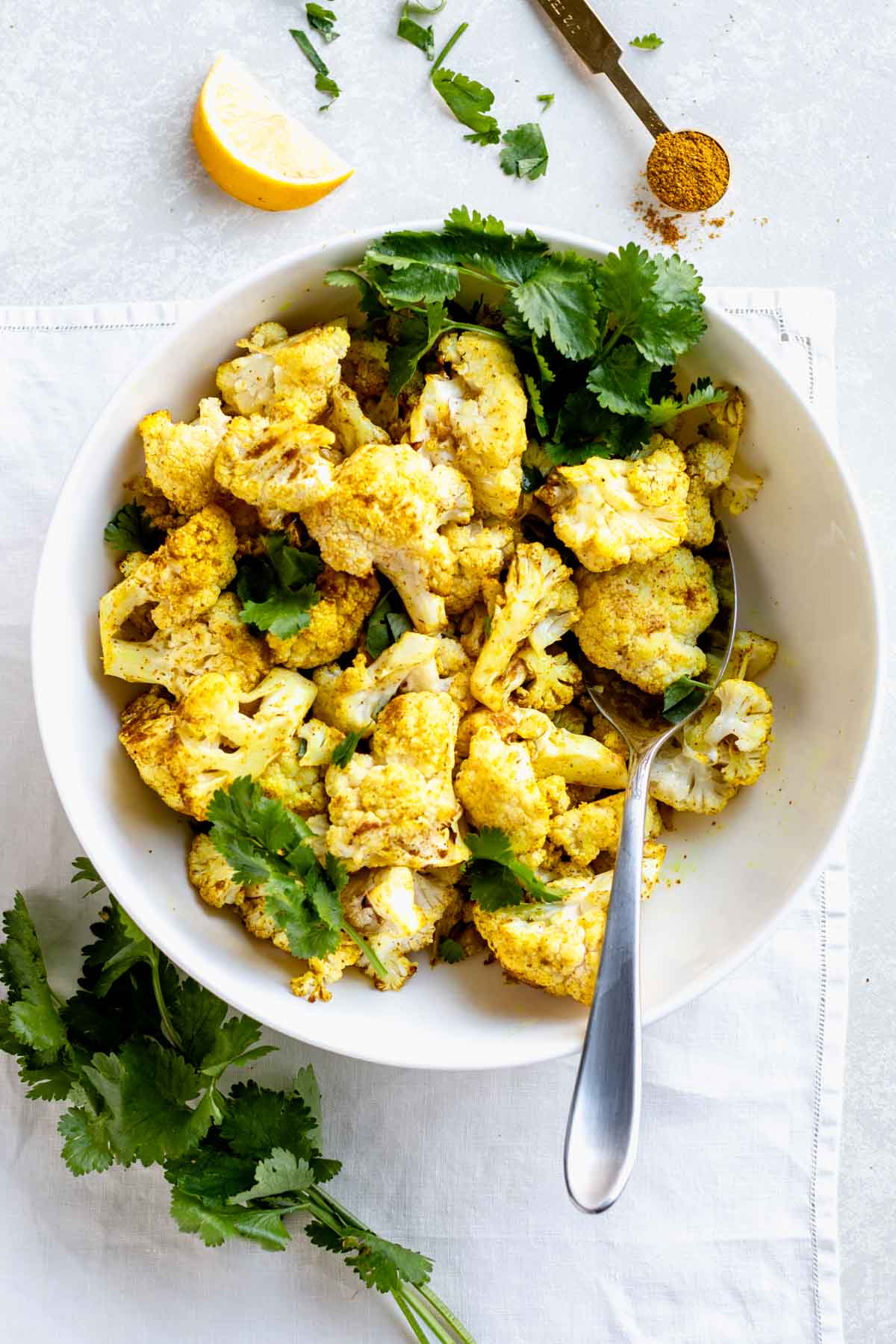 curry cauliflower in a white bowl with cilantro sprigs