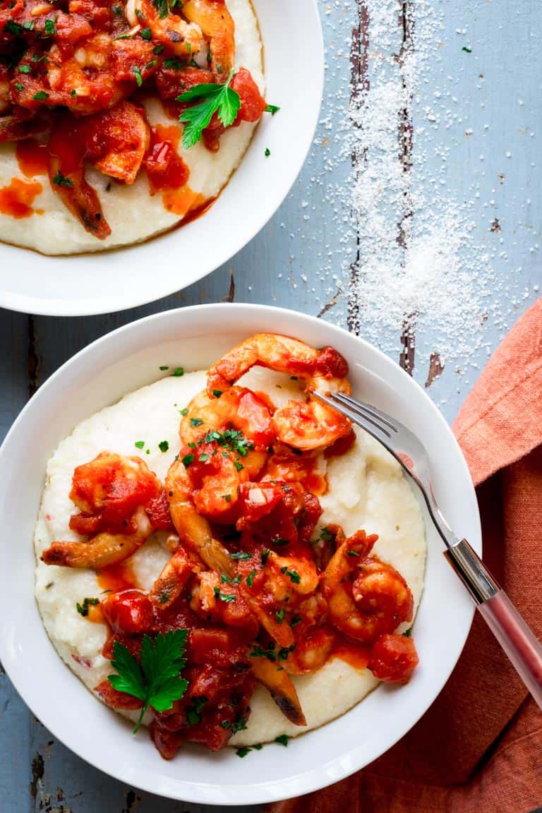 Two bowls of Spicy Shrimp and Cheese Grits on a blue surface with a linen and a fork
