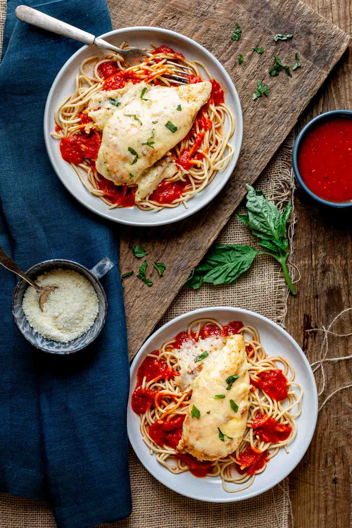 two plates of spaghetti with chicken parmesan and sauce on top