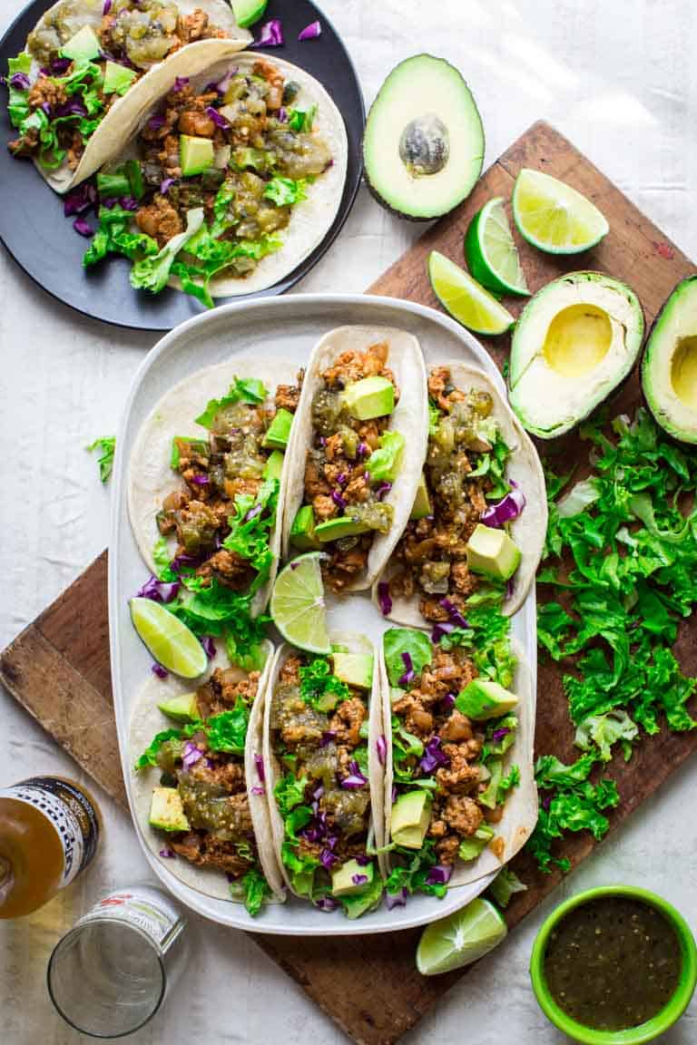 a platter of tacos and cutting board with avocado and lettuce