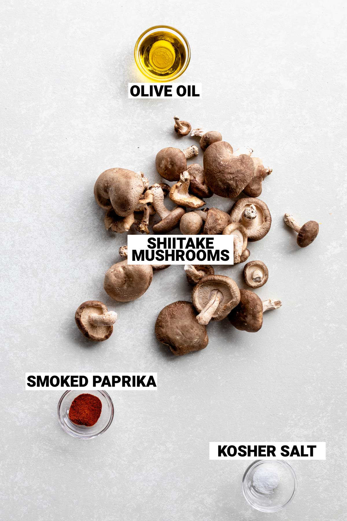 Shiitake mushrooms on a table with a small bowl of oil and a small bowl of paprika next to them.