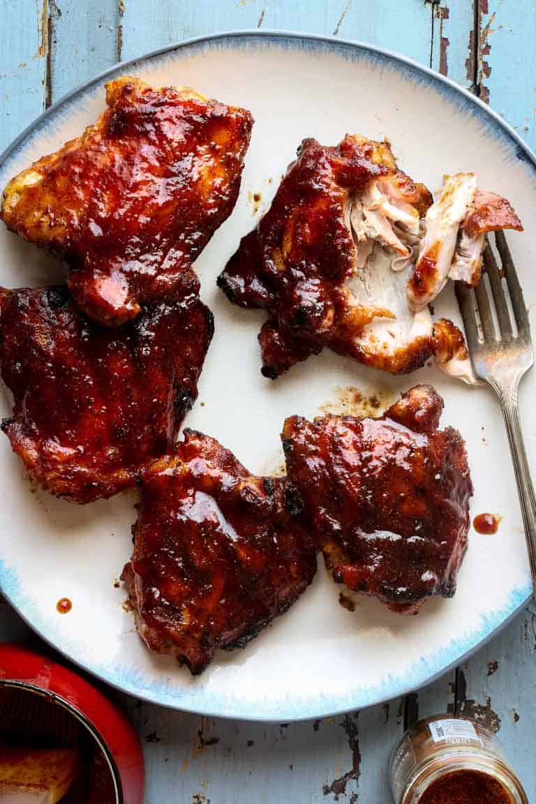 a platter of barbecue chicken with a fork tearing into one of them showing the inside of the cooked chicken