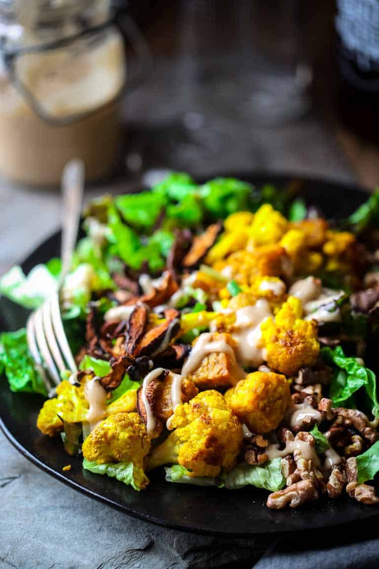 close up shot of turmeric roasted cauliflower and vegan bacon over salad, drizzled with dressing