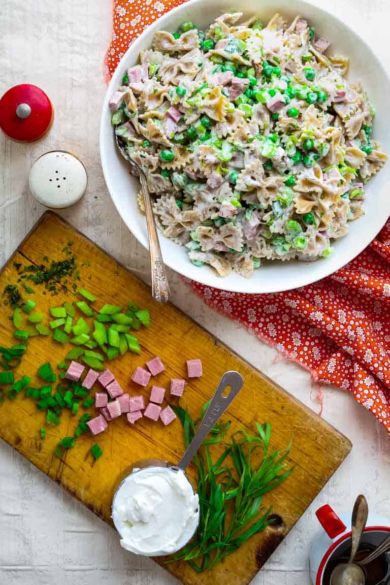 overhead of pasta salad with peas and ham and a cutting board with peas and ham on it