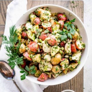 closeup overhead of potato salad in a white bowl with herb sprigs