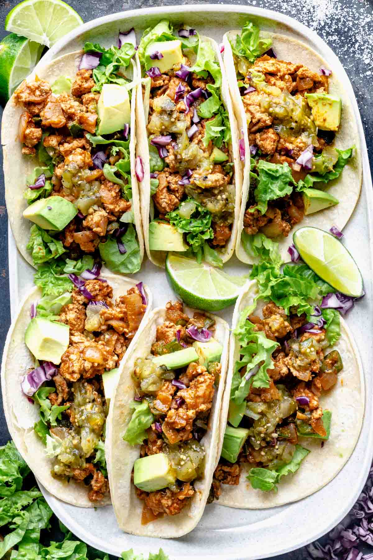a platter of chicken tacos with lime, avocado, and poblano peppers
